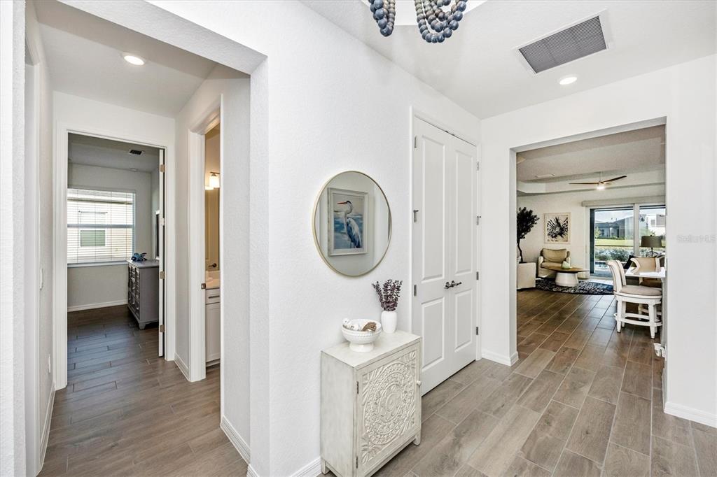 A bright entryway features wood-look tile flooring, a white console table, and a round mirror — 12950 TULUM LOOP, VENICE, FL