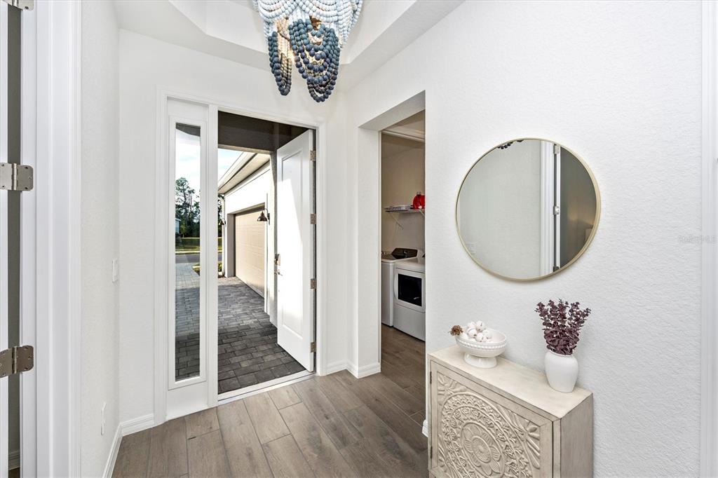 An entryway features wood-look tile flooring, a blue beaded chandelier, and a round wall mirror — 12950 TULUM LOOP, VENICE, FL