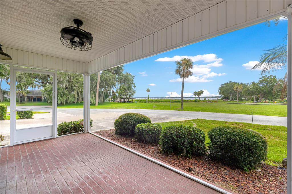 A covered brick patio with a ceiling fan overlooks a grassy lawn and a lake — 925 BEVERLY HARBORS DRIVE, LEESBURG, FL
