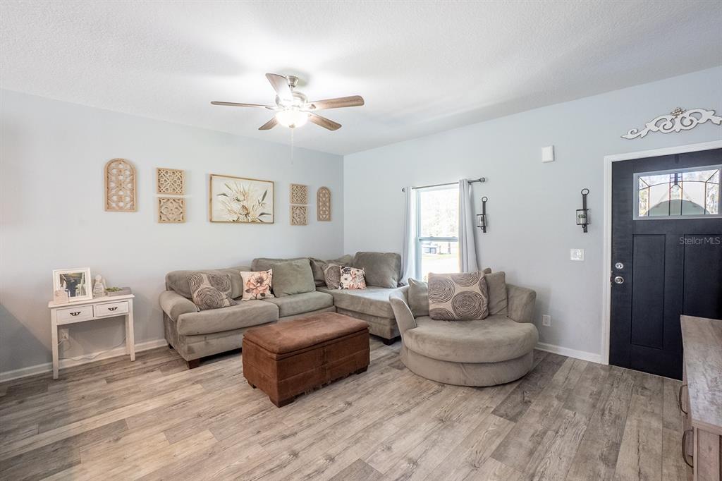 A living room features light blue walls, wood-look flooring, a sectional sofa, and a ceiling fan — 10410 ZIGLER AVENUE, HASTINGS, FL