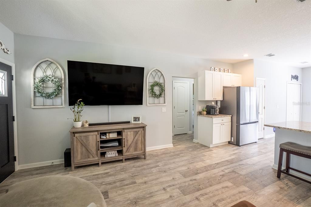 A living room with a wall-mounted television, wooden media console, and an adjacent kitchen area — 10410 ZIGLER AVENUE, HASTINGS, FL