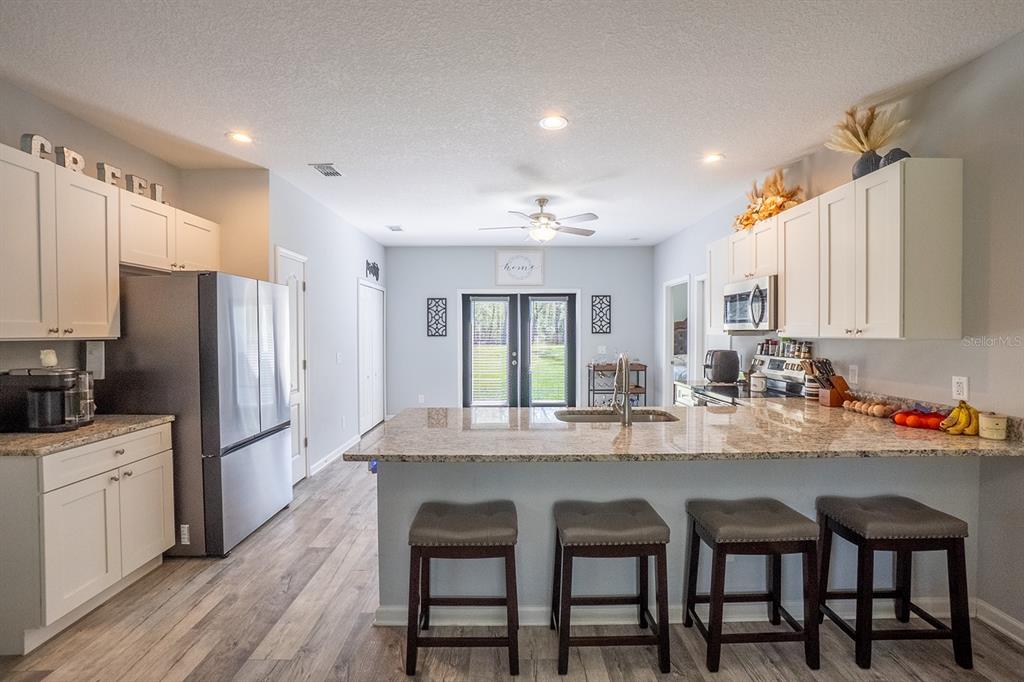 A kitchen with white cabinets, granite countertops, a large island with bar stools, and stainless appliances — 10410 ZIGLER AVENUE, HASTINGS, FL