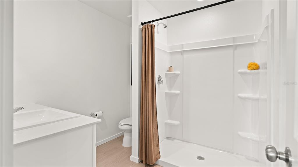 A bathroom features a white vanity, a toilet, and a shower stall with a brown curtain — 2102 PARSLEY DRIVE, HAINES CITY, FL