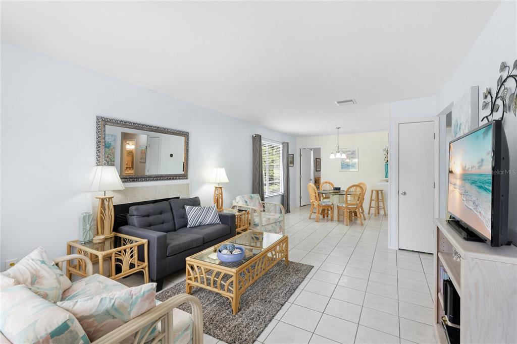A living room with white tile floors, a grey sofa, and a dining area beyond — 3634 59TH AVENUE W, BRADENTON, FL