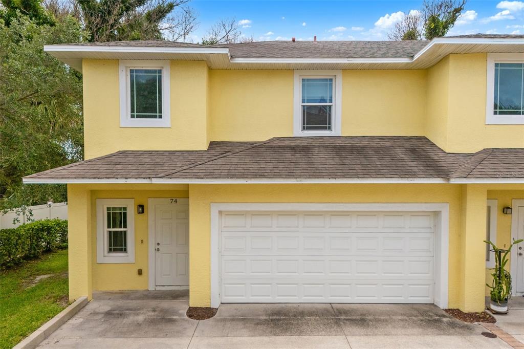 A two-story yellow townhouse exterior features a white garage door and a front entry door — 74 JUNE DRIVE, COCOA BEACH, FL