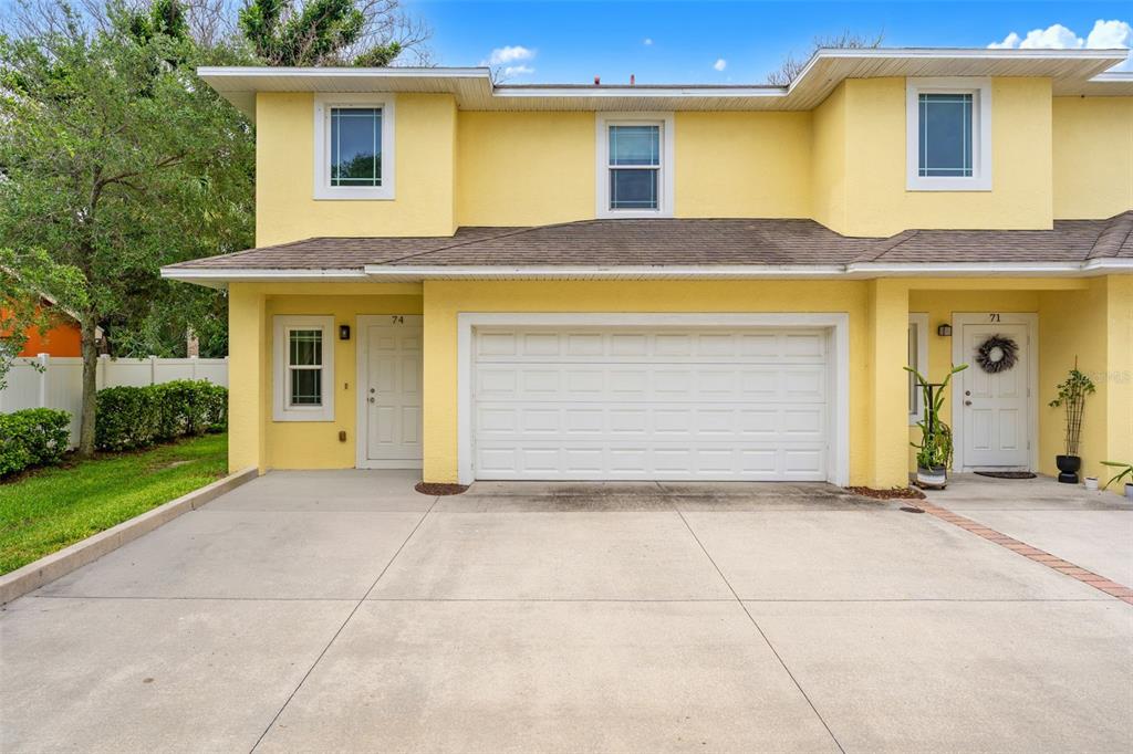 A two-story yellow townhouse with a white garage door and a concrete driveway — 74 JUNE DRIVE, COCOA BEACH, FL