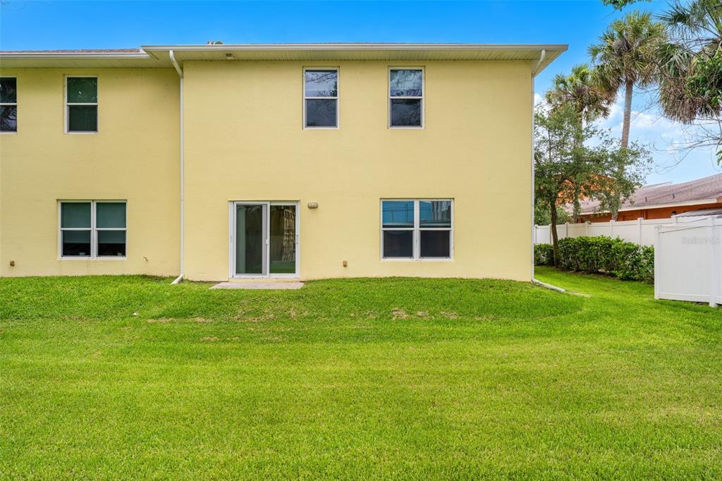 The exterior of a two-story yellow building features a sliding glass door and green lawn — 74 JUNE DRIVE, COCOA BEACH, FL
