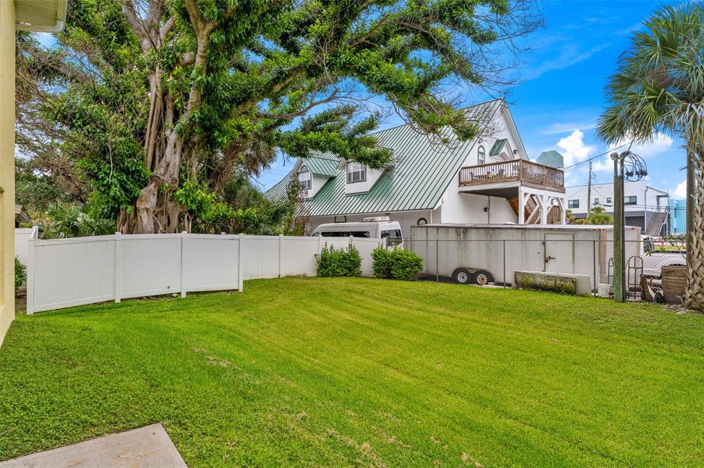 A grassy backyard features a white vinyl fence, a large tree, and a nearby house — 74 JUNE DRIVE, COCOA BEACH, FL