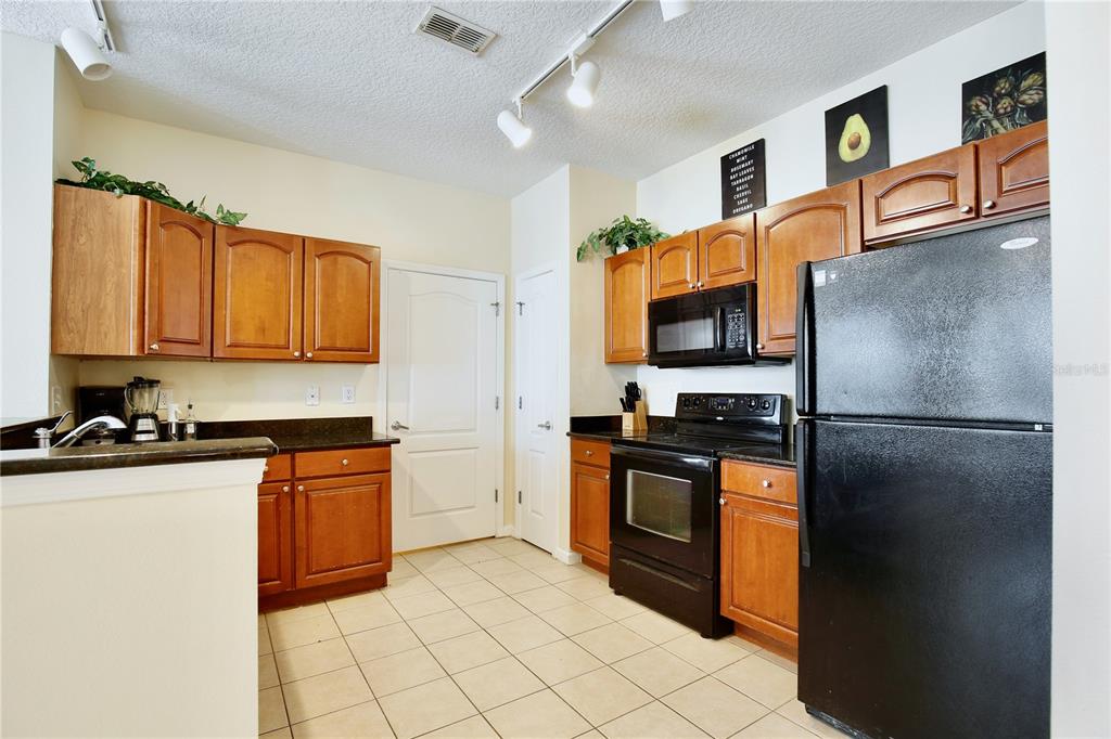 A kitchen features wood cabinets, black appliances, dark countertops, and light tile flooring — 5255 CANE ISLAND LOOP UNIT 204, KISSIMMEE, FL