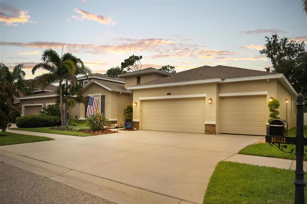 A tan single-story house with a three-car garage and a landscaped front yard at sunset — 10321 RIVERDALE RISE DRIVE, RIVERVIEW, FL