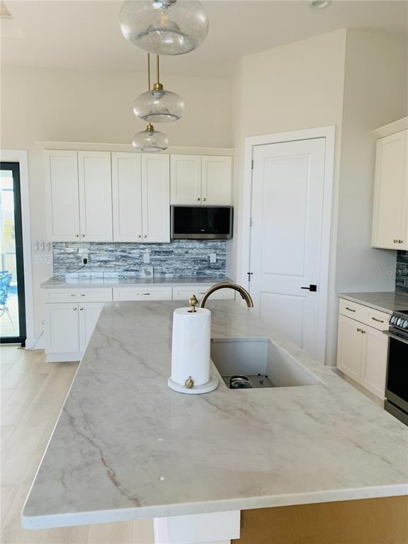 A kitchen features white cabinetry, a marble-topped island with a sink, and a stone backsplash — 703 BOUNDARY BOULEVARD, ROTONDA WEST, FL