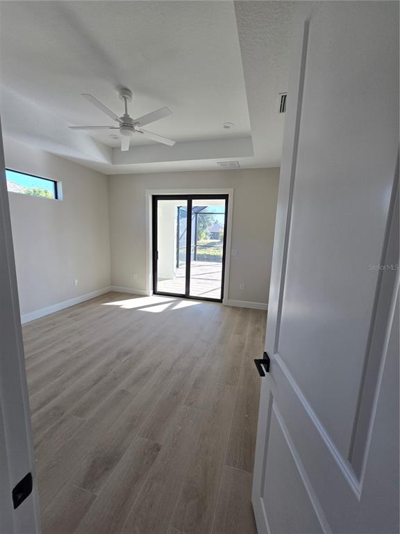 A bedroom with light wood-look flooring, a tray ceiling, and sliding glass doors to a patio — 703 BOUNDARY BOULEVARD, ROTONDA WEST, FL