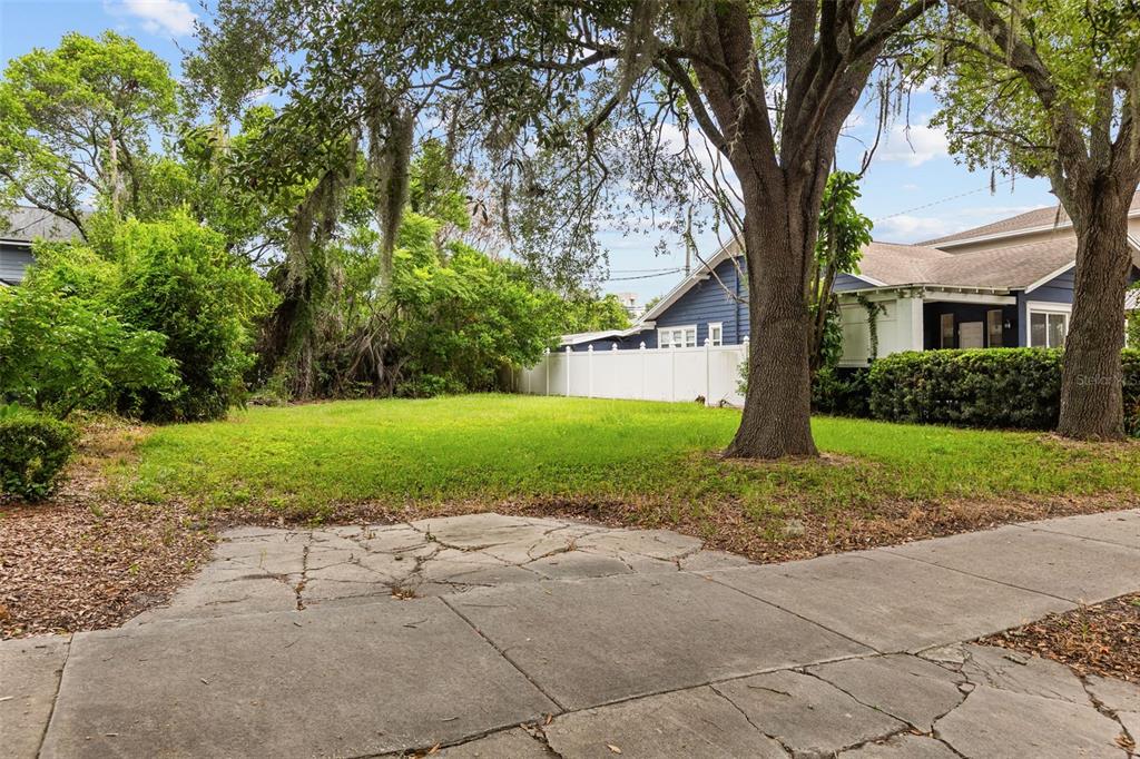 A vacant grassy lot sits between mature trees and a white fence next to a house — 311 E YALE STREET, ORLANDO, FL
