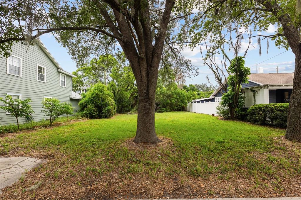 A grassy backyard lot sits between two houses, featuring a large central tree — 311 E YALE STREET, ORLANDO, FL