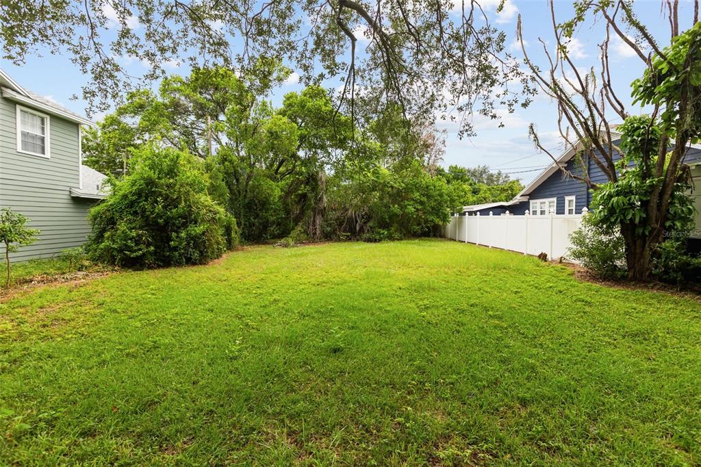 A grassy backyard is framed by a light green house, a dark blue house, and trees — 311 E YALE STREET, ORLANDO, FL
