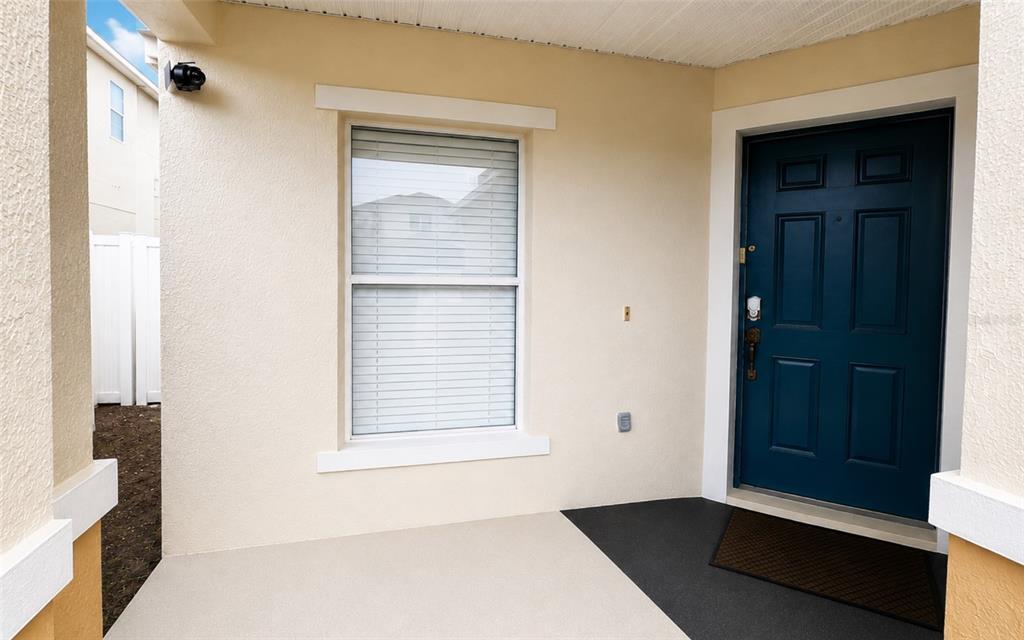 A covered entryway features a blue front door, a single window, and a security camera — 133 RONA LANE, DAVENPORT, FL