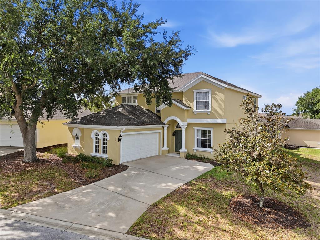 A two-story yellow house features a concrete driveway, a large tree, and arched windows — 353 PLUMOSO LOOP, DAVENPORT, FL