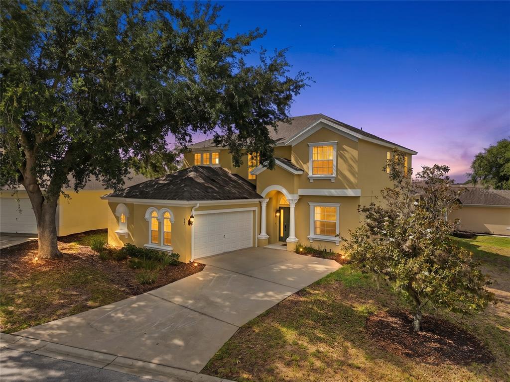 A two-story yellow house with a two-car garage and a paved driveway at dusk — 353 PLUMOSO LOOP, DAVENPORT, FL