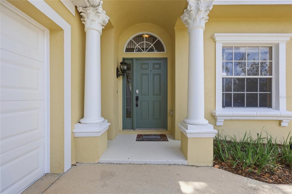 The exterior entrance features a green front door flanked by white columns and a window — 353 PLUMOSO LOOP, DAVENPORT, FL