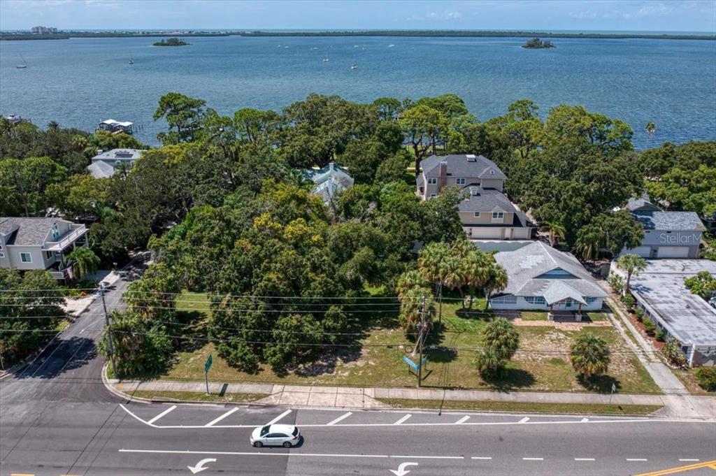 An aerial view shows a vacant lot with trees situated between houses near the water — 1040 BROADWAY, DUNEDIN, FL