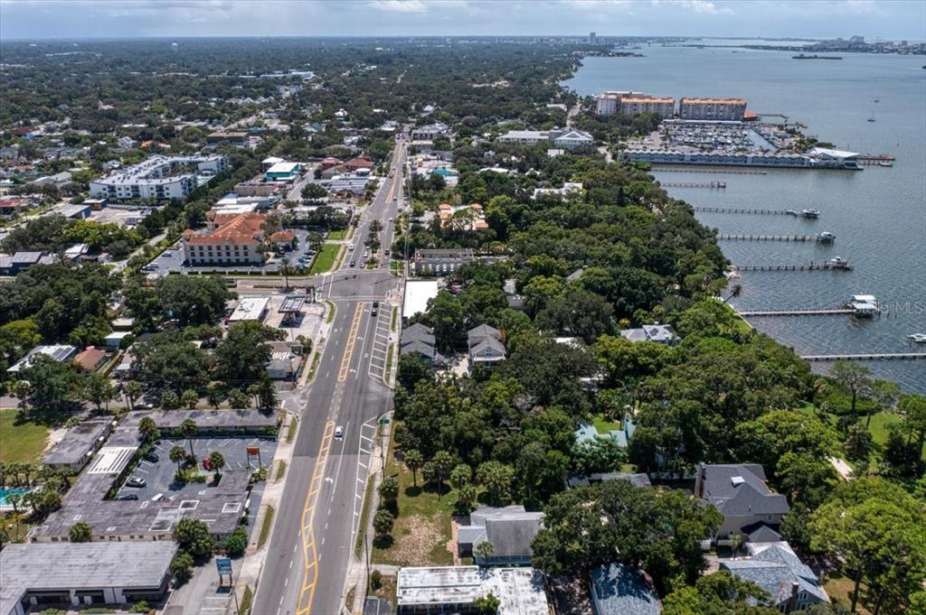An aerial view shows a coastal town with a main road, buildings, and boat docks — 1040 BROADWAY, DUNEDIN, FL