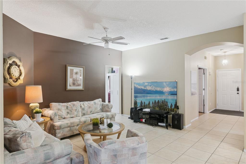 A living room features a brown accent wall, tiled floors, a ceiling fan, and furniture — 765 JAYBEE AVENUE, DAVENPORT, FL