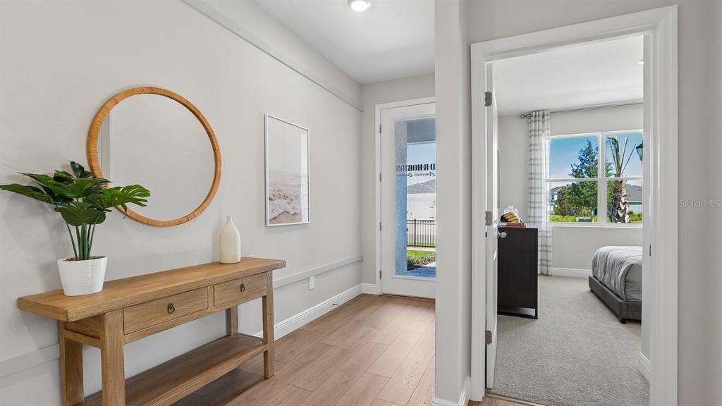 A hallway with wood-look flooring leads to an exterior door and an adjacent carpeted bedroom — 35596 BRICK CHURCH LOOP, DADE CITY, FL