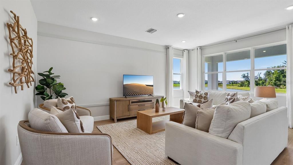 A bright living room features a television, light-colored furniture, a wooden coffee table, and windows — 35596 BRICK CHURCH LOOP, DADE CITY, FL
