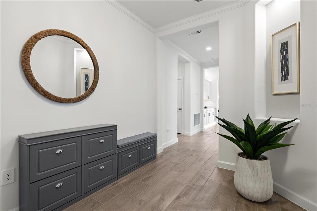 A hallway features a gray storage bench, a round mirror, and a potted plant — 5144 SPOTTED SEAL LANE, BRADENTON, FL