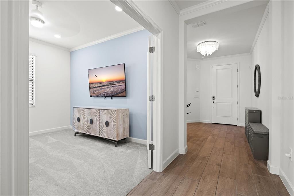 A carpeted room with a television and cabinet connects to a tiled entryway with a door — 5144 SPOTTED SEAL LANE, BRADENTON, FL