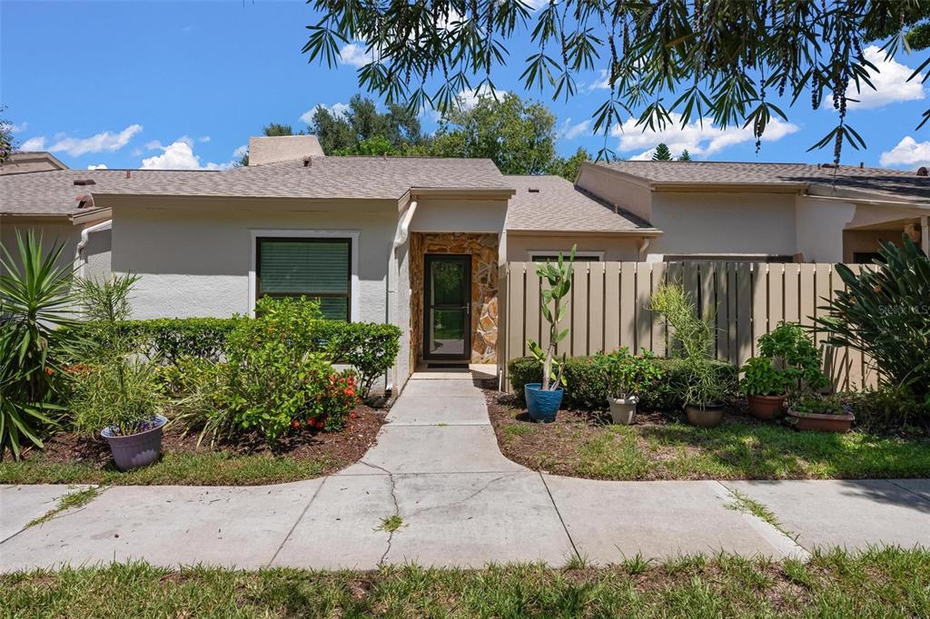 A single-story house exterior features a stone-accented entryway, a concrete walkway, and potted plants — 1554 TALLYWOOD DRIVE UNIT 7127, SARASOTA, FL