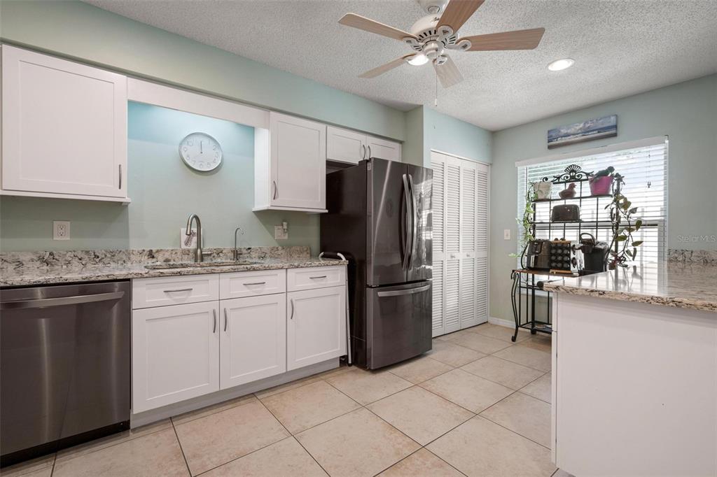 A kitchen features white cabinets, granite countertops, stainless steel appliances, and light-colored tile flooring — 1554 TALLYWOOD DRIVE UNIT 7127, SARASOTA, FL