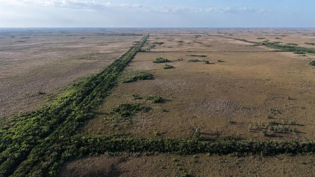An aerial view shows a vast, flat landscape of dry grasses and scattered green shrubs — 0 UNKNOWN ROAD, HOMESTEAD, FL