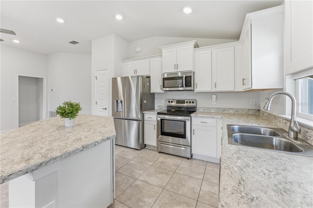 An open-concept living room and kitchen with white cabinets, tile flooring, and a ceiling fan — 111 KRENSON BAY LOOP, WINTER HAVEN, FL