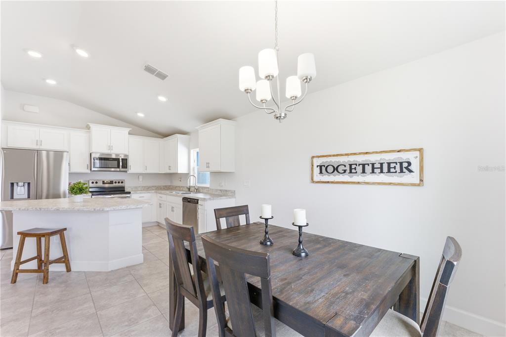 An open-concept kitchen and living area featuring white cabinets, stainless appliances, and tile flooring — 111 KRENSON BAY LOOP, WINTER HAVEN, FL