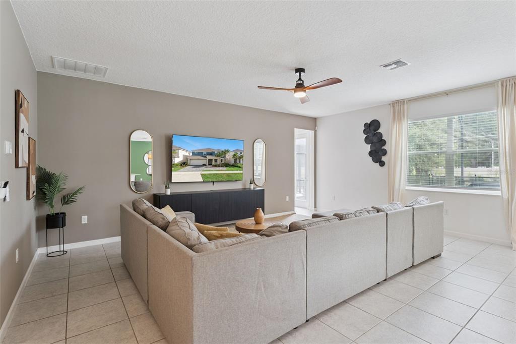 A living room features a large sectional sofa, a wall-mounted television, and tile flooring — 302 MARCELLO BOULEVARD, KISSIMMEE, FL