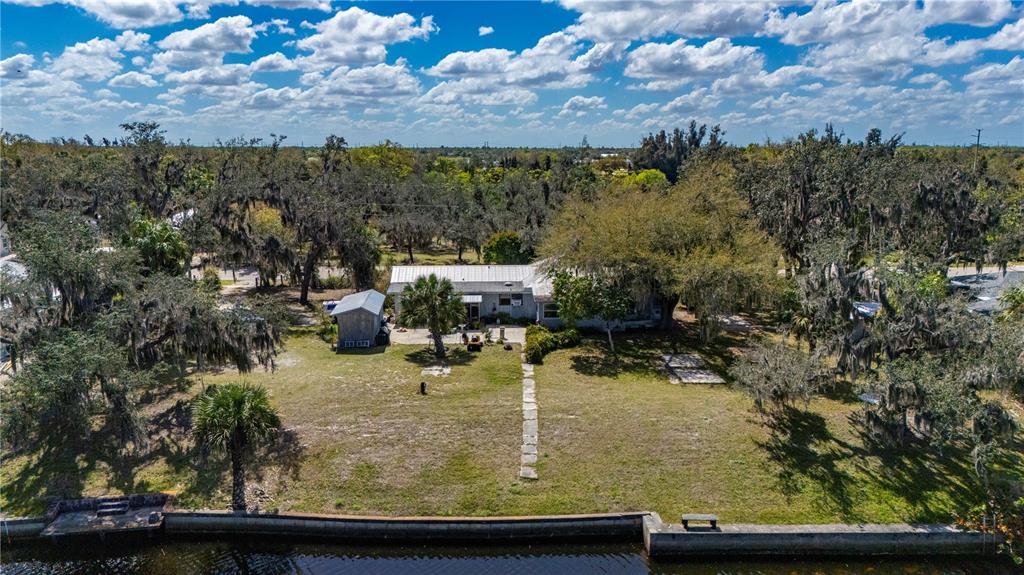 An aerial view of a waterfront house with a large yard, trees, and a shed — 7754 RIVERSIDE DRIVE, PUNTA GORDA, FL