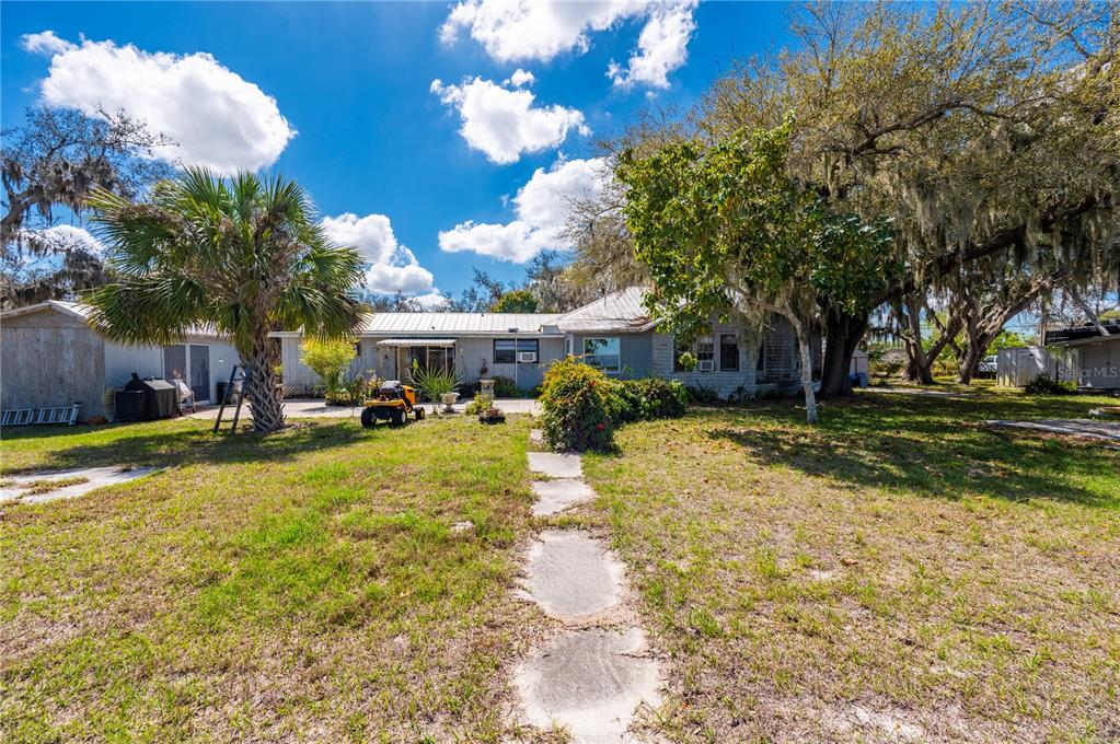 A backyard view of a single-story house with a palm tree and stone path — 7754 RIVERSIDE DRIVE, PUNTA GORDA, FL