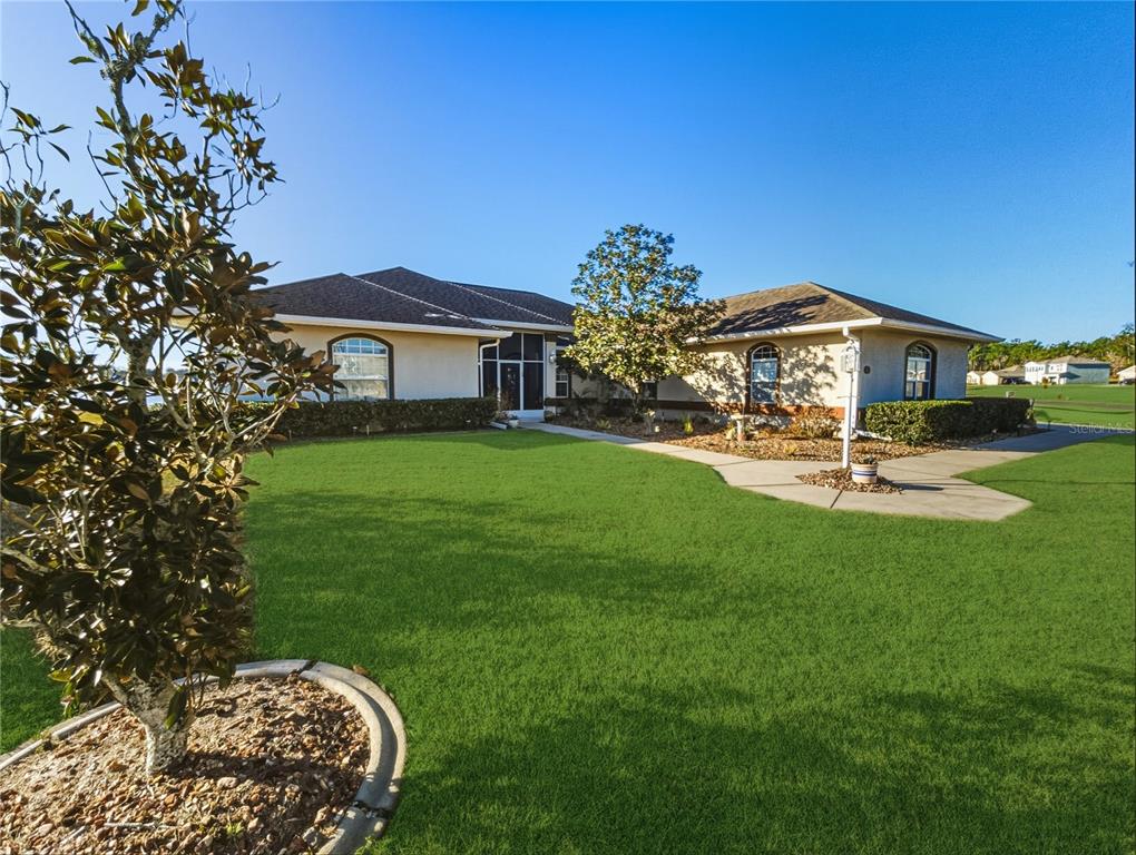 A single-story house with a large lawn, a concrete walkway, and a screened-in entryway — 77 HICKORY LOOP, OCALA, FL