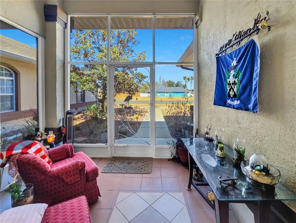 A sunroom features a red armchair, a glass-topped console table, and a screen door — 77 HICKORY LOOP, OCALA, FL