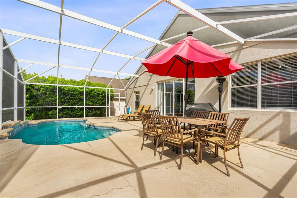 A screened-in patio features a swimming pool, a dining set with a red umbrella, and lounge chairs — 208 TROON CIRCLE, DAVENPORT, FL
