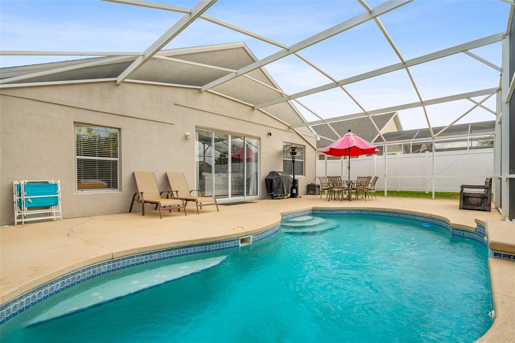 A swimming pool with a screened-in lanai, patio furniture, and a house exterior — 208 TROON CIRCLE, DAVENPORT, FL