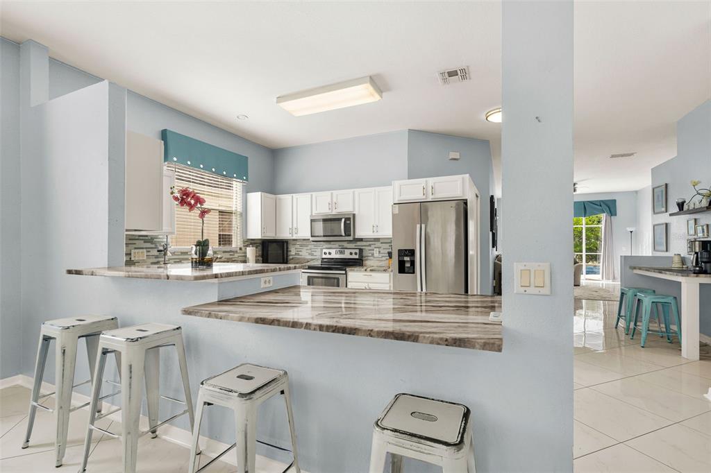 A kitchen features light blue walls, white cabinets, stainless steel appliances, and a breakfast bar — 208 TROON CIRCLE, DAVENPORT, FL