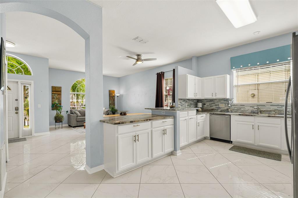 A kitchen with white cabinets and granite countertops opens into a living room with tile floors — 208 TROON CIRCLE, DAVENPORT, FL