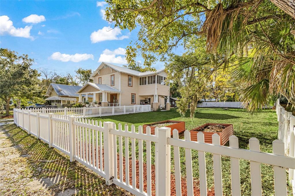 A two-story tan house with a white picket fence and raised garden beds in the yard — 213 N MONROE AVENUE, ARCADIA, FL