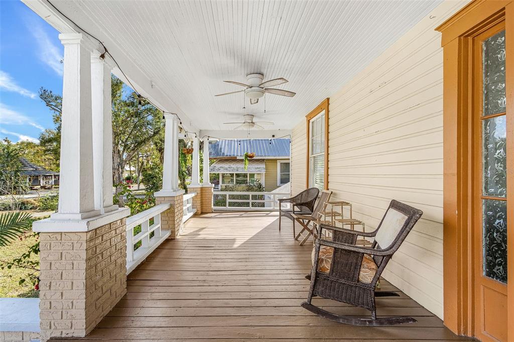 A covered wooden porch features white columns, brick bases, ceiling fans, and wicker rocking chairs — 213 N MONROE AVENUE, ARCADIA, FL