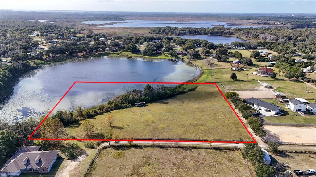 An aerial view shows a large lake surrounded by grassy fields, trees, and residential houses — 000 KENNY TRAIL, EUSTIS, FL