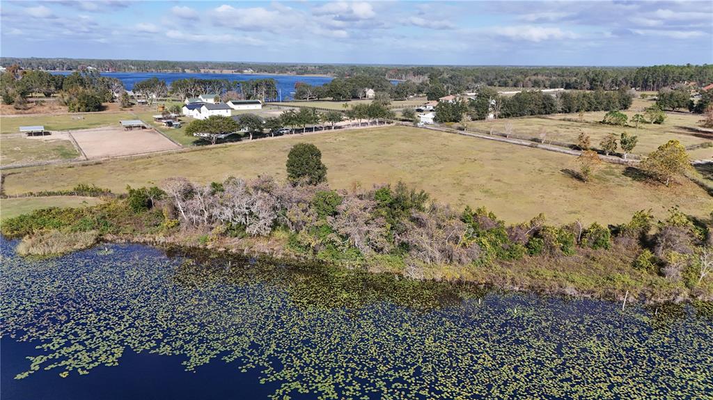 An aerial view shows a grassy property with fenced paddocks, outbuildings, and a lakefront — 000 KENNY TRAIL, EUSTIS, FL