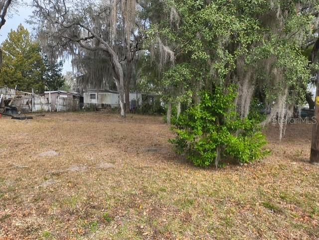 A grassy, tree-filled lot with a mobile home visible in the background — 4734 N APACHE TRAIL, HERNANDO, FL