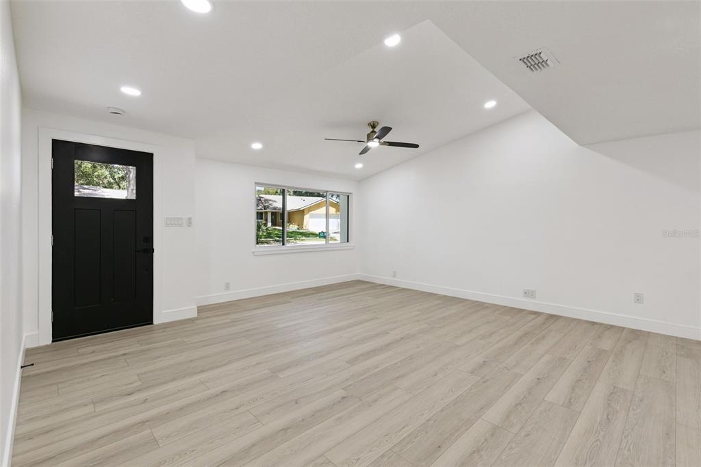 A bright, empty room features white walls, light wood-look flooring, a ceiling fan, and a black door — 141 MILL RUN DRIVE, LAKE MARY, FL